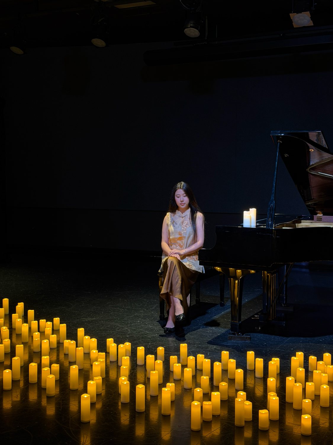 Hellena Yang seated at a grand piano surrounded by candles
